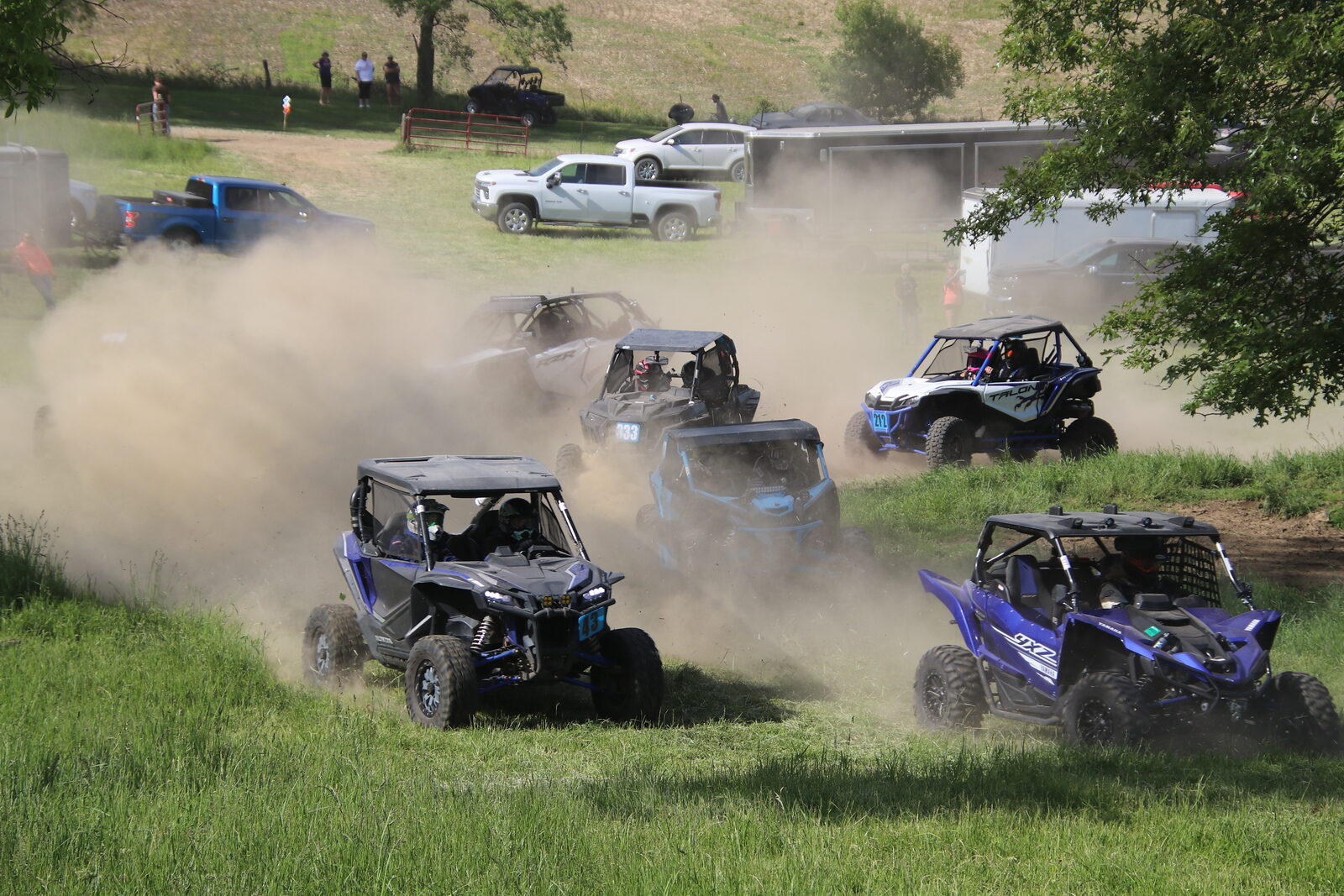 A pack of UTVs kicking up dust racing through an open field